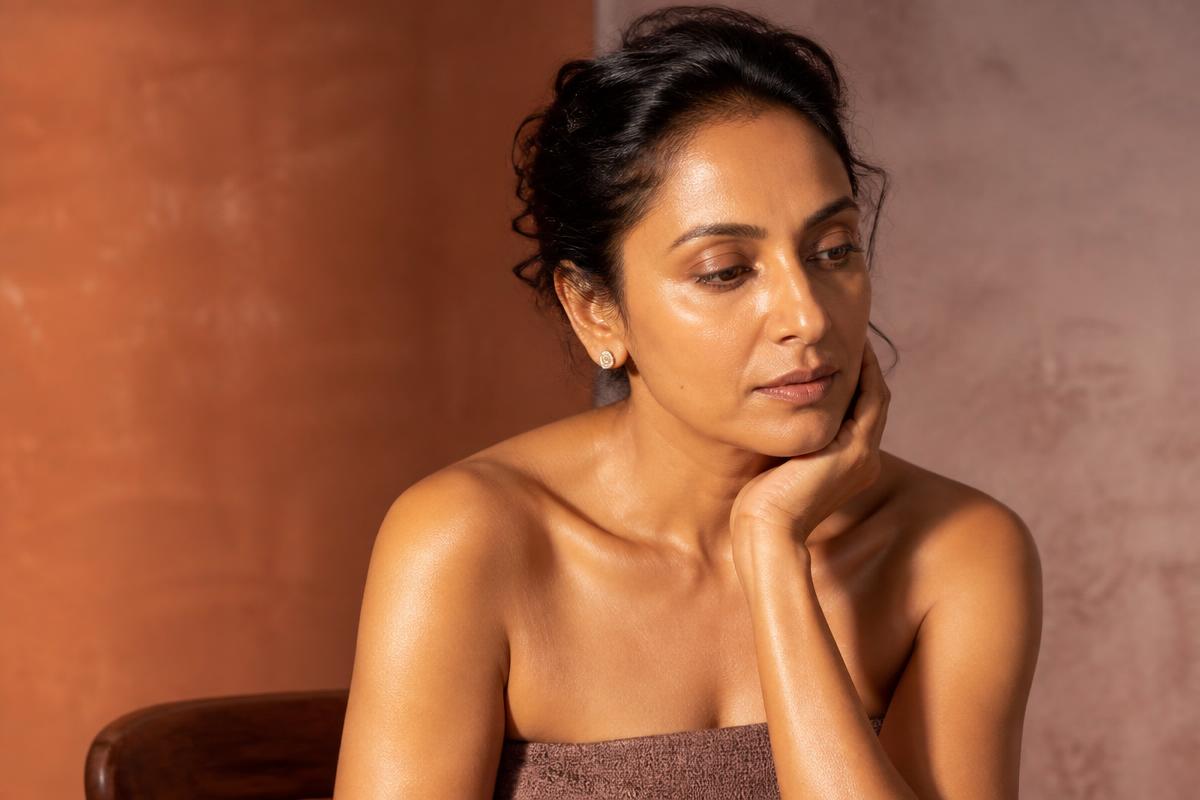 A Brown woman in her fifties resting a hand near her cheek in soft daylight